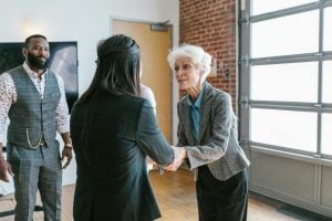 Three people in a modern office space, two women are shaking hands, while a man stands nearby observing.