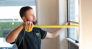 A man measuring a window using a tape measure for a Brisbane company specializing in window tinting.