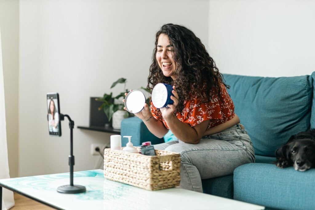 An influencer is sitting on a couch with her dog, using her online presence to make money.