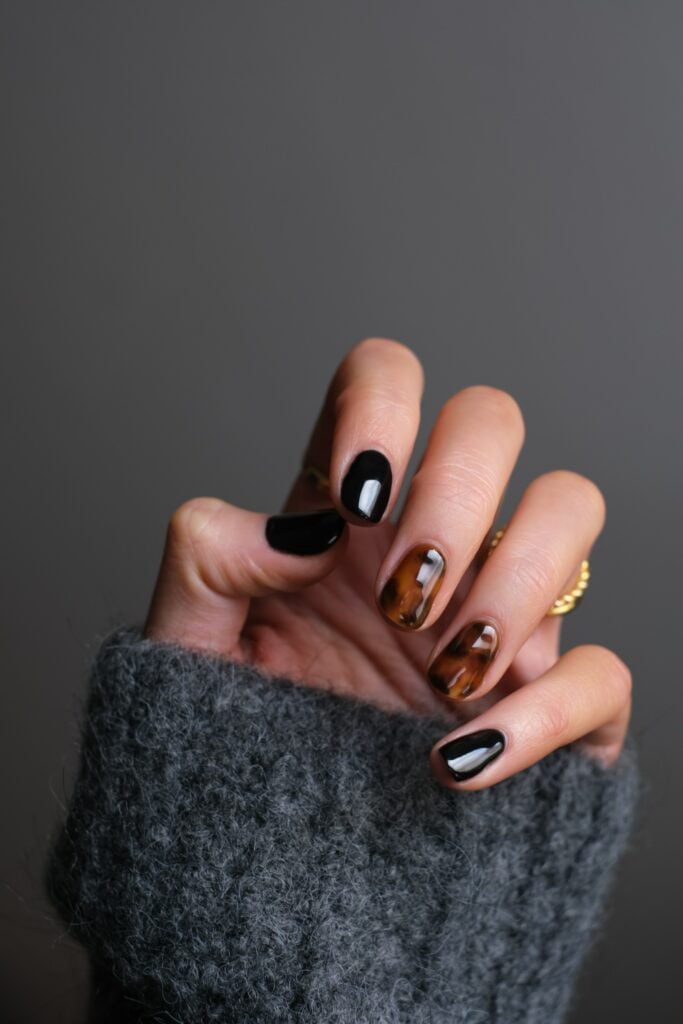 A woman's hand showcasing stunning black and brown nail polish. With expertise in nail art and nail care techniques, learn how to become a nail tech and unlock endless possibilities for creativity and self-expression
