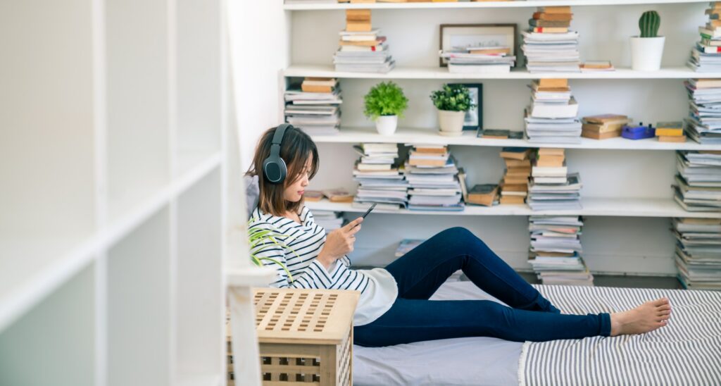 A woman is sitting on a bed in a room surrounded by an extensive collection of books.