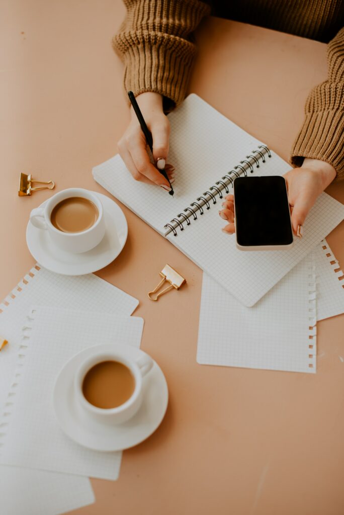 A woman, focused and determined, is mastering the art of ambition as she gracefully writes on a notebook while holding a cup of coffee.