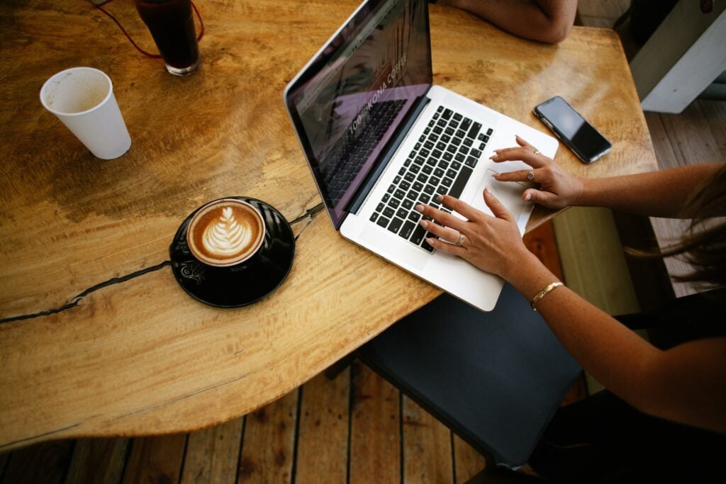 A woman typing on a laptop at a coffee shop while working on a business case.