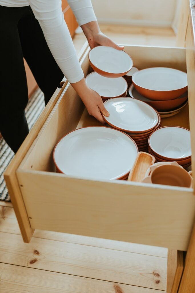 A woman is organizing plates in a drawer.