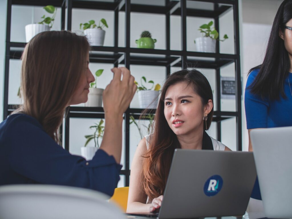 A group of women sitting around a table with laptops, discussing content ranking strategies and trends in SEO for 2023.