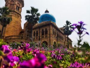 A large building adorned with a blue dome and surrounded by vibrant purple flowers.
