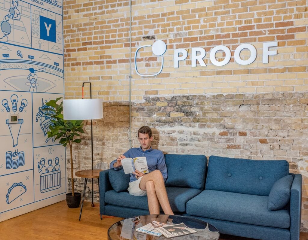 A man leveraging dynamic web crawling techniques, sitting on a blue couch in a room with a brick wall.