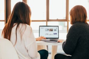 Two women studying digital marketing and SEO trends while sitting at a table with a laptop.