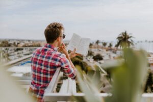 Keywords: business performance, customer experience

Description: A man reading a book on a balcony overlooking the ocean while harnessing email address intelligence to boost business performance and enhance customer experience.