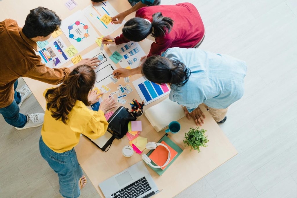 Top view of a group of people collaborating around a table with charts, papers, and a laptop, engaging in a brainstorming session focused on digital marketing strategies.