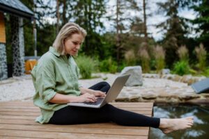 A woman sitting on a dock with a laptop, researching proven Google Ads strategies for NDIS businesses.
