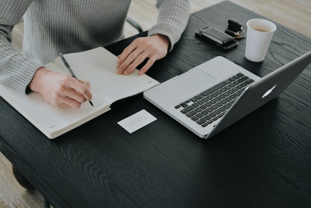 A person diligently typing on a laptop at a desk, engrossed in researching and jotting down notes on "Cornell Notes" - the ultimate note-taking method that promises enhanced comprehension and