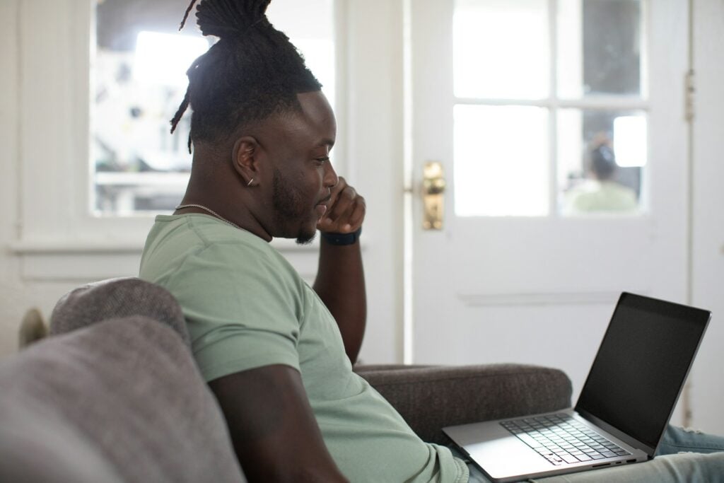 An idle man deeply diving into his laptop while sitting on a couch.