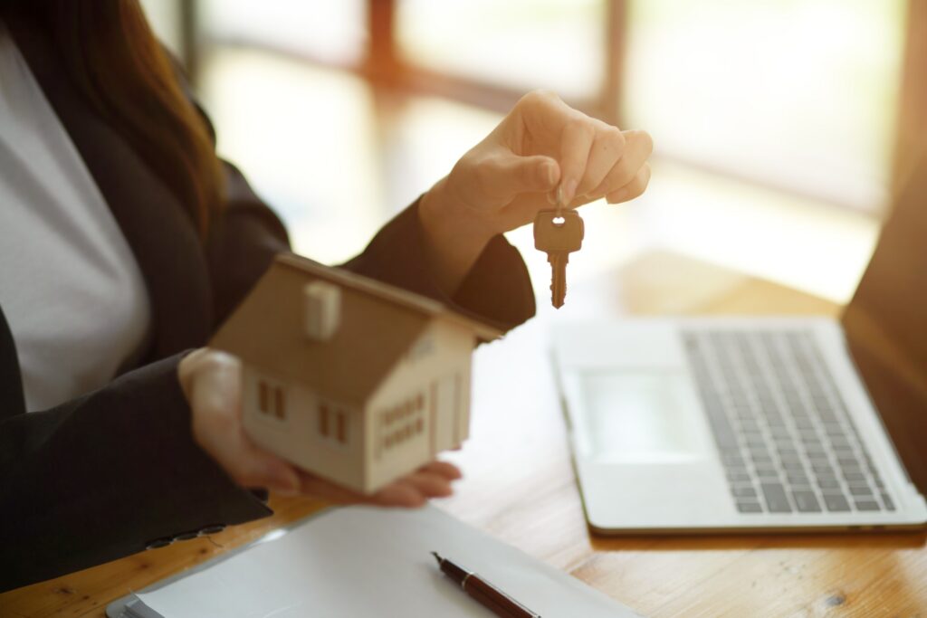 A woman holding a model of a house next to a laptop offers a complete guide on reverse mortgages for beginners.