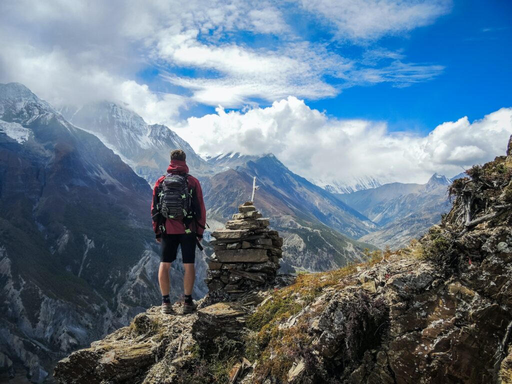 A man standing on top of a cliff, backpacking in the mountains.