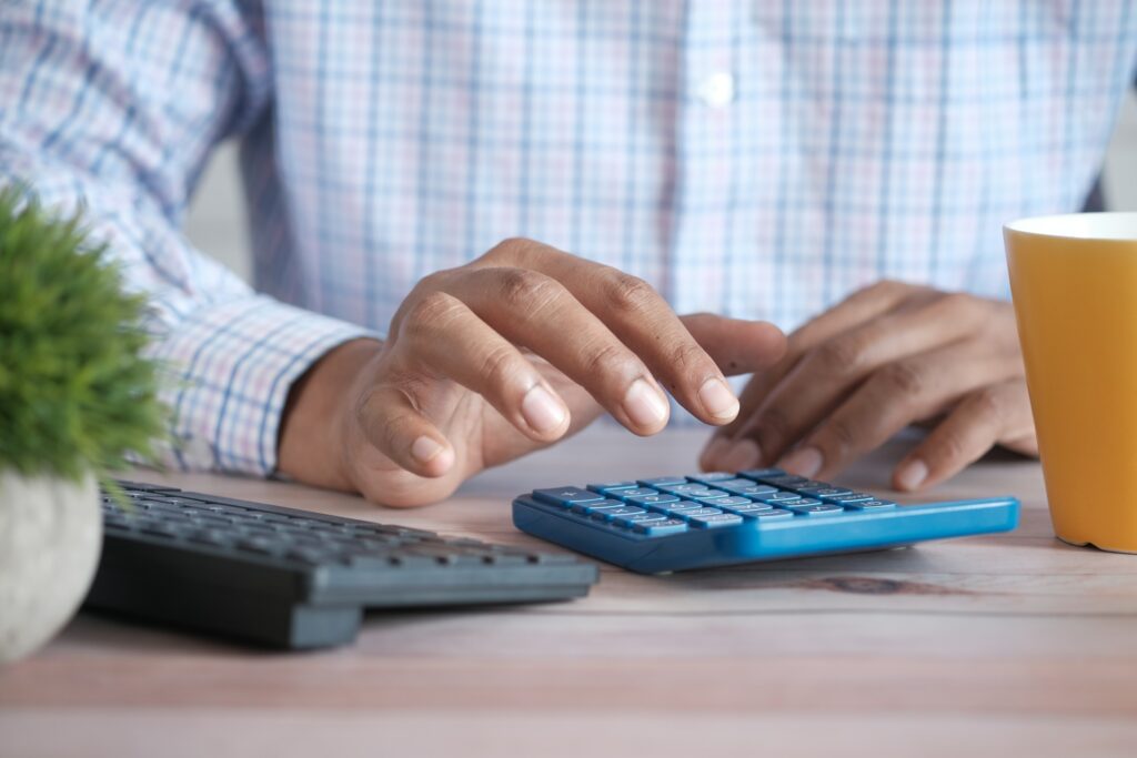 A man conducting a comprehensive exploration of gross income while using a calculator on a desk.