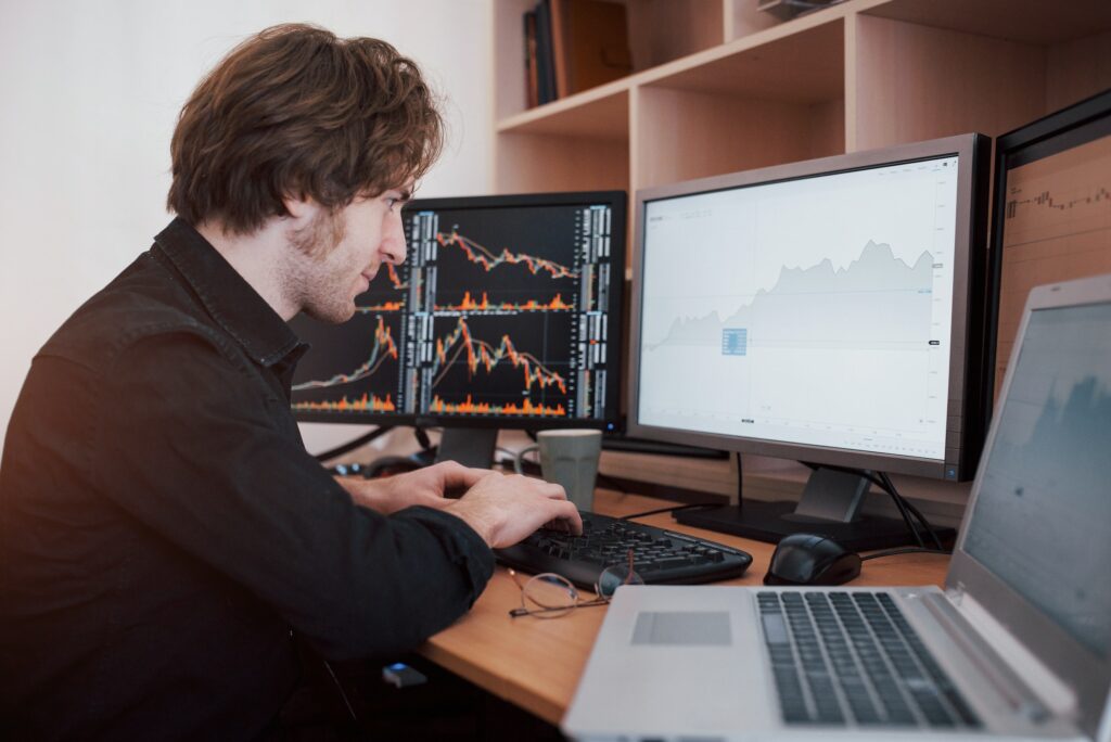 A man studying market failure at a desk with multiple screens.