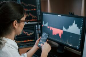 A woman is studying a stock chart on a computer screen, referring to the contrarian's playbook for potential short selling opportunities.