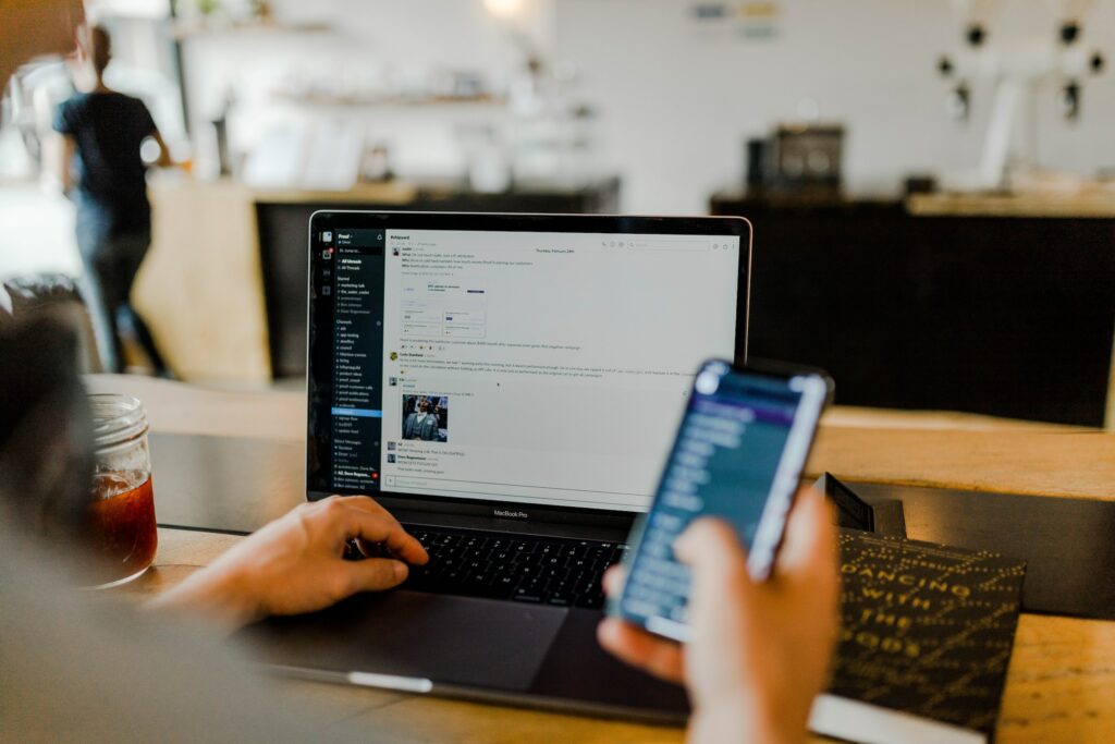 A Person Sitting At A Table With A Laptop And Cell Phone, Exploring &Quot;What Is Slack.