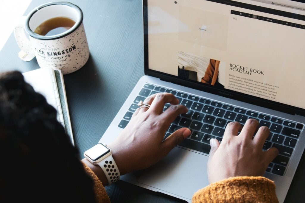 A woman typing on a laptop while sipping coffee, exploring the question "What is Squarespace?