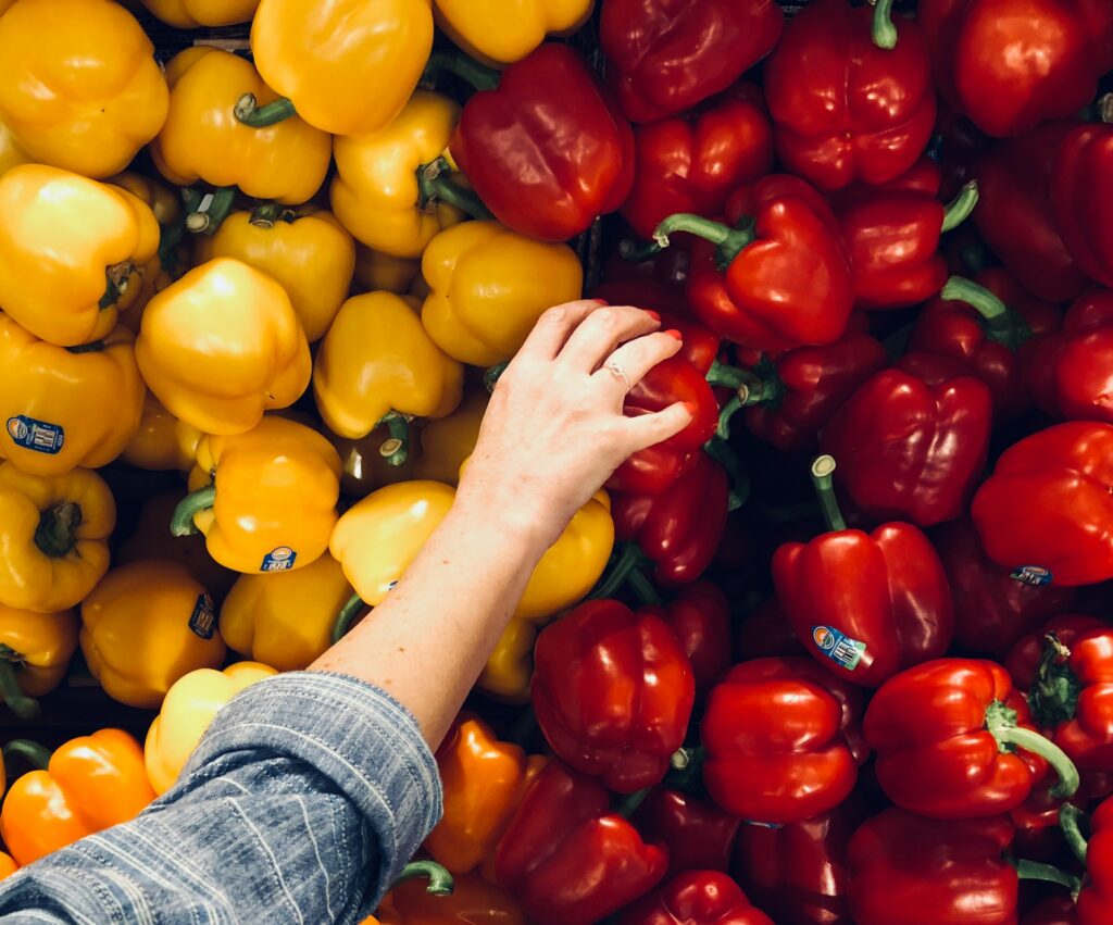A person's hand reaching into a pile of red and yellow peppers, symbolizing health and sustainability. (Thrive Market)